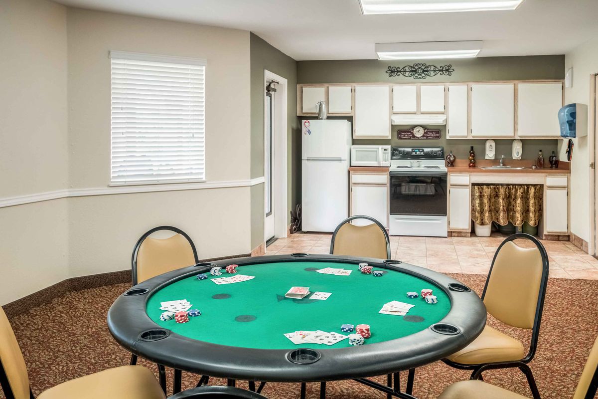 A poker table with playing cards in a room featuring a kitchen area with appliances.