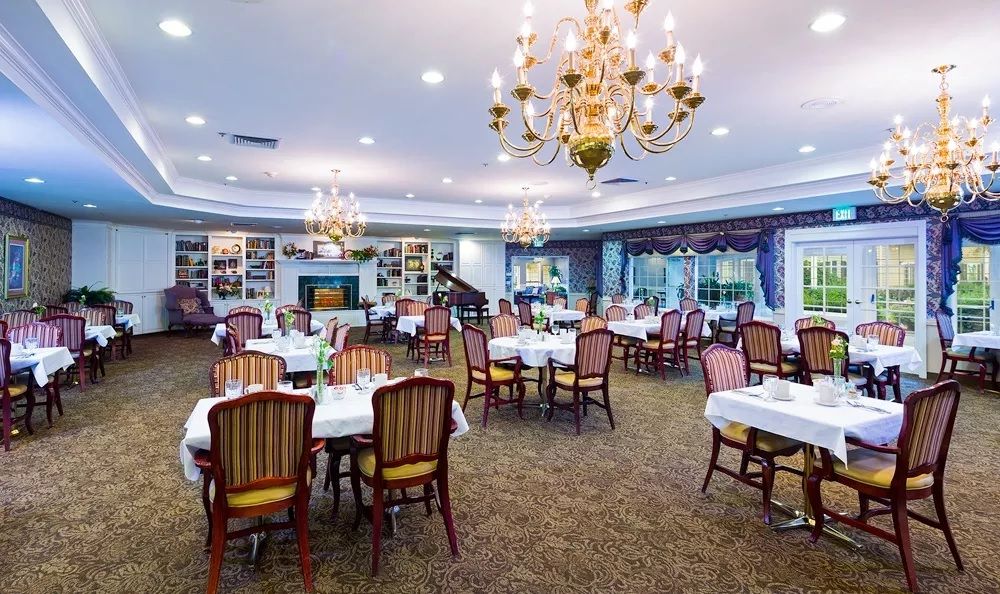An elegant dining room with chandeliers, set with multiple tables and chairs.