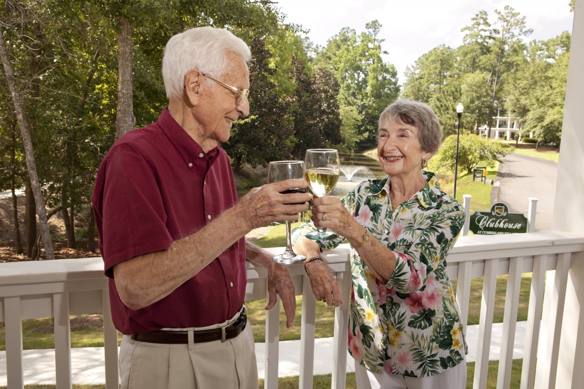 An elderly couple enjoying a toast together on a sunny day outdoors.