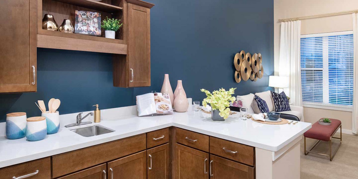 A modern kitchen with wooden cabinets, a white countertop, and decorative vases against a blue wall.