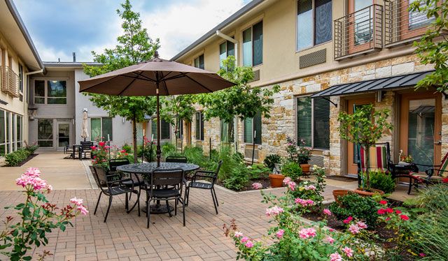 A charming courtyard with outdoor seating, featuring a table with an umbrella surrounded by lush greenery and blooming flowers.
