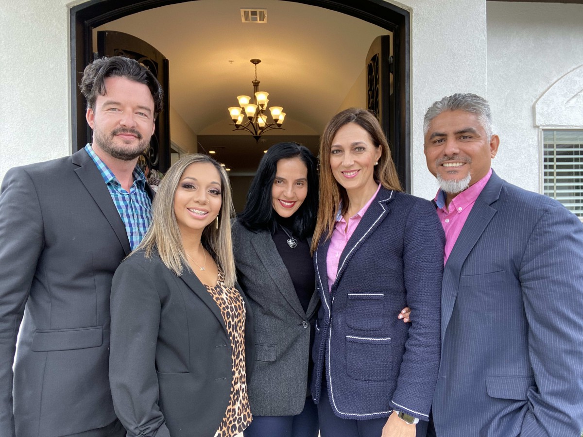 A group of five people dressed in business attire, smiling and standing together.