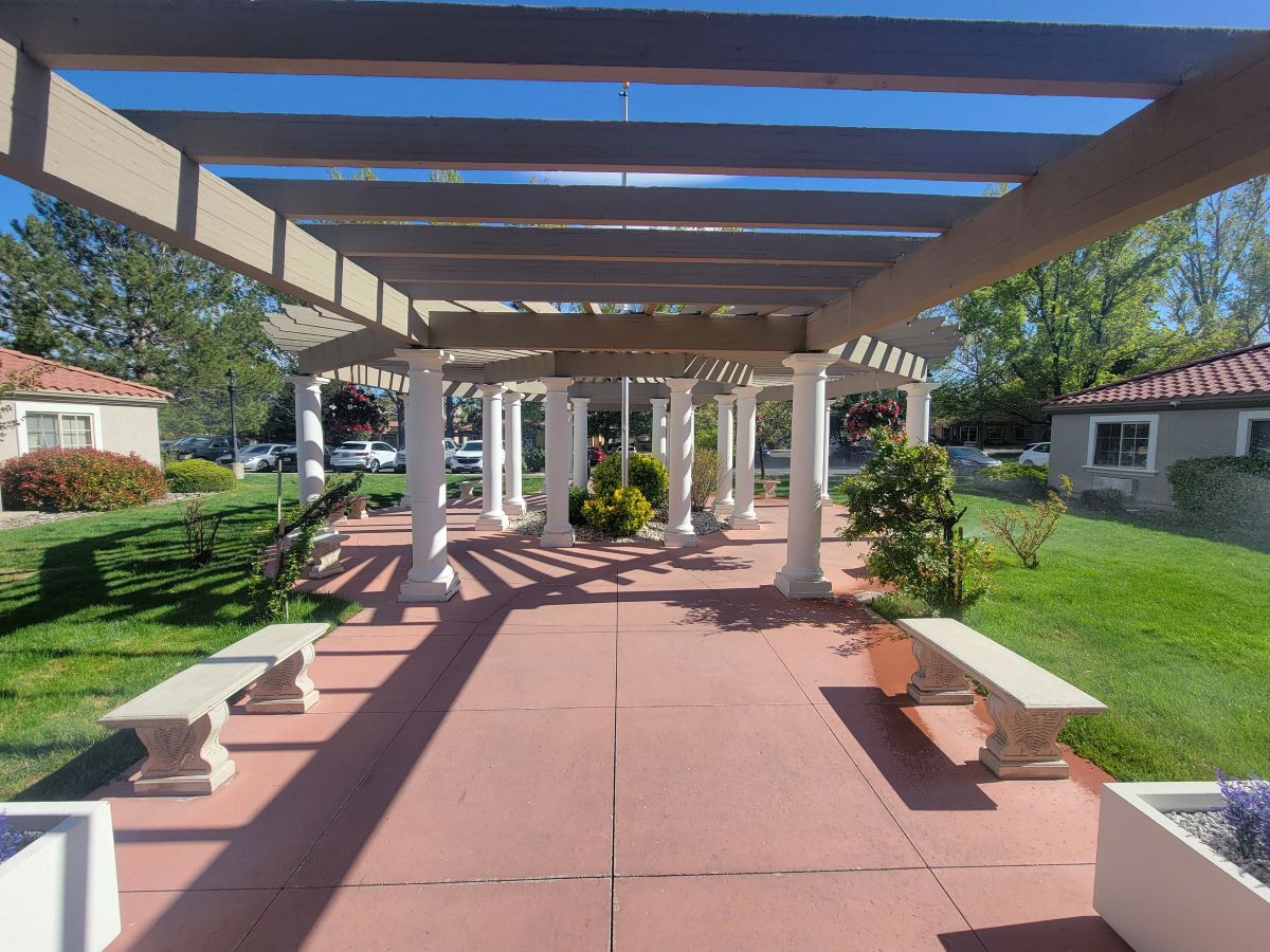 A scenic outdoor pergola with benches surrounded by a garden setting.