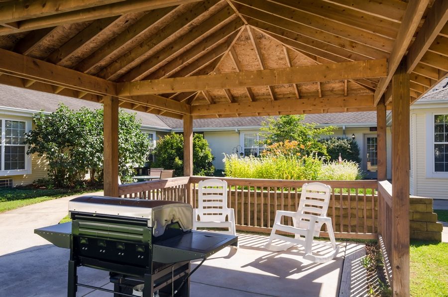 A cozy outdoor gazebo with a barbecue grill and seating area, surrounded by greenery.
