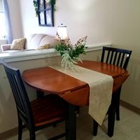 A cozy dining area featuring a wooden table and chairs, adorned with a floral centerpiece and table runner.