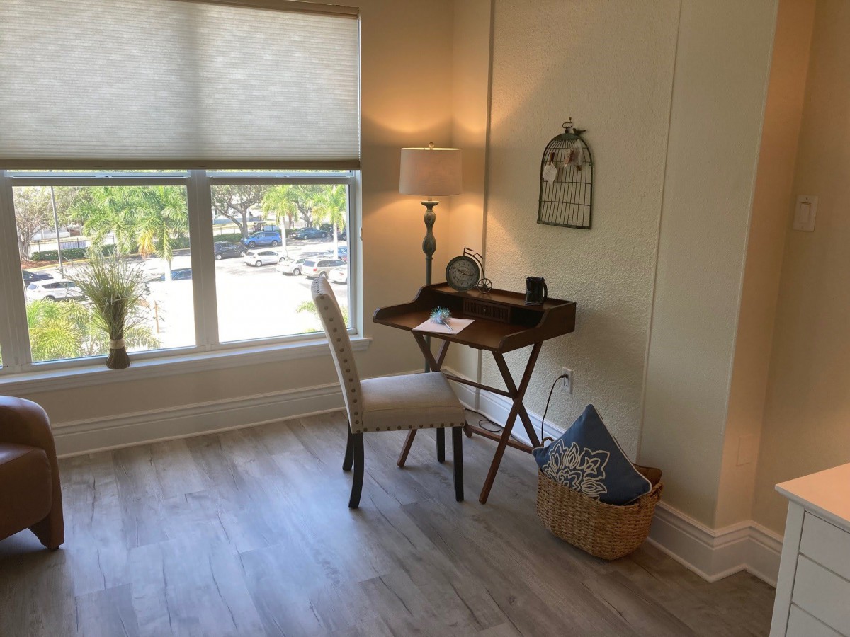 A cozy home office corner with a small wooden desk and chair beside a large window.