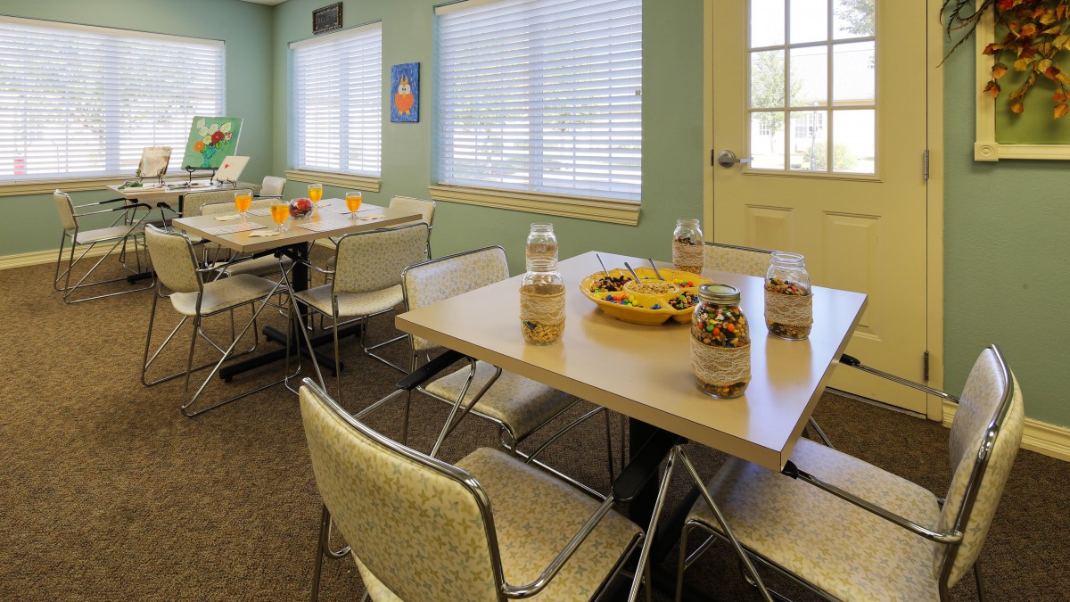 A community dining area with tables set up with snacks and chairs around them.