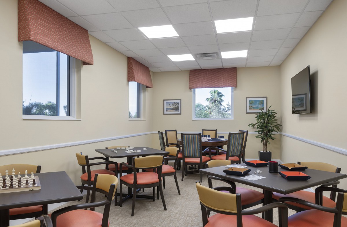 A well-lit dining room with multiple tables and chairs, featuring large windows and wall decorations.