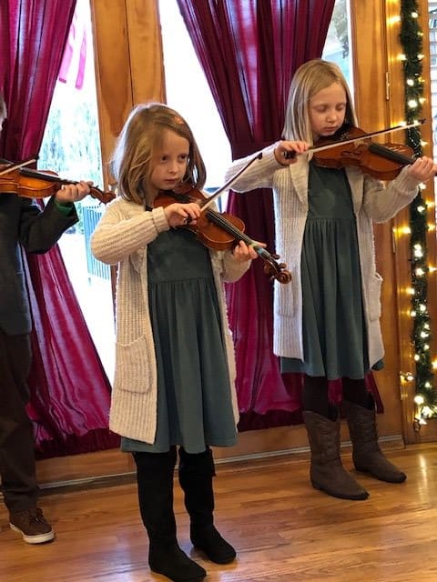 Children performing with violins during an indoor concert.