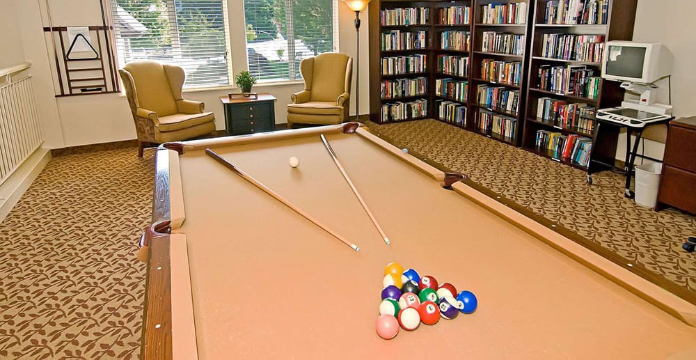 A cozy game room with a pool table and a library area featuring bookshelves and comfortable chairs.