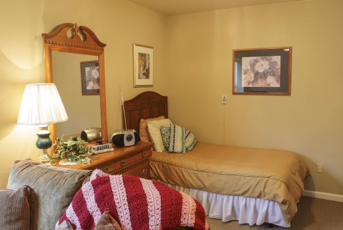 A cozy bedroom with a neatly made bed, decorative pillows, and a wooden dresser with a mirror.