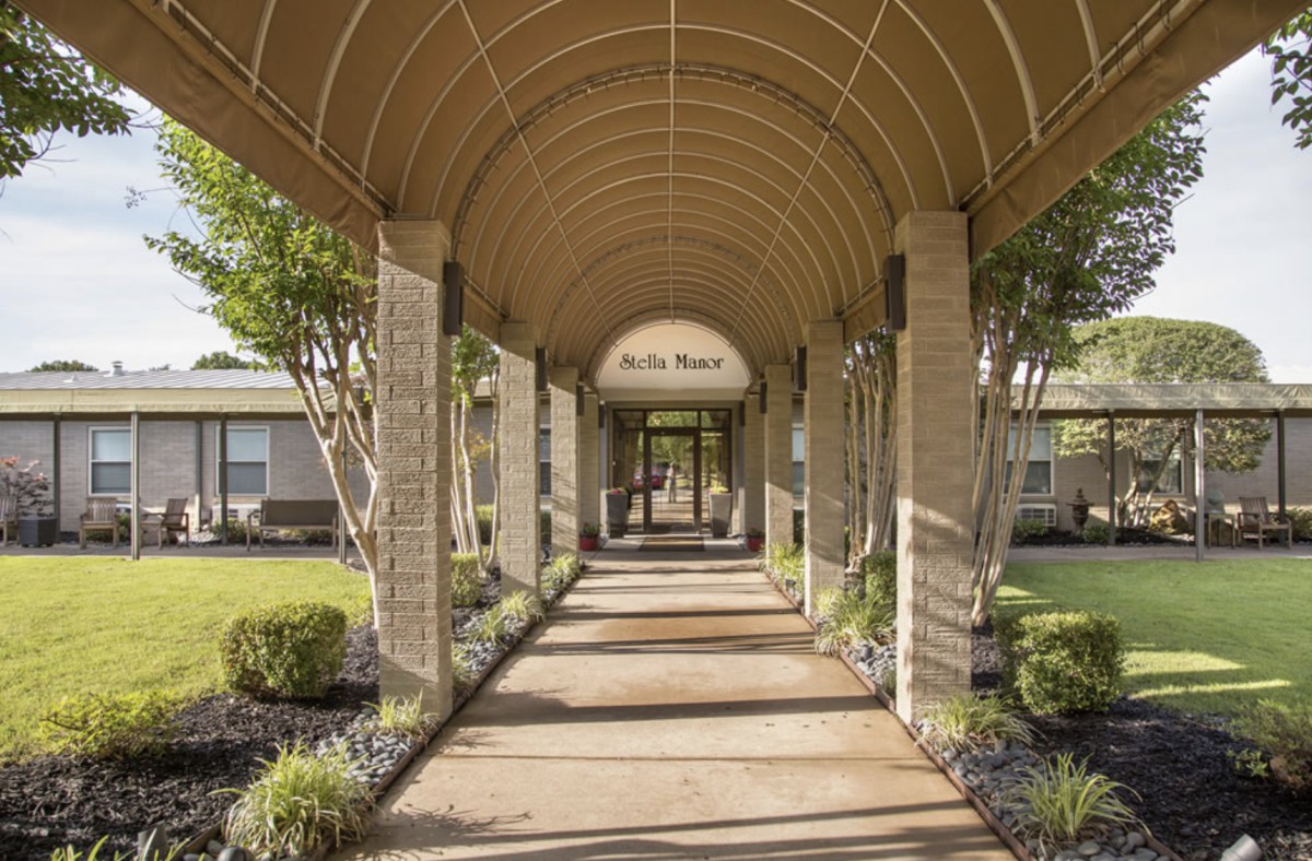 Covered walkway leading to a building entrance surrounded by greenery.