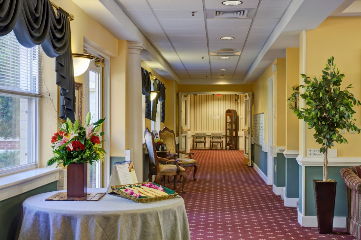 A traditionally decorated hallway featuring a red carpet, elegant chairs, and floral arrangements.