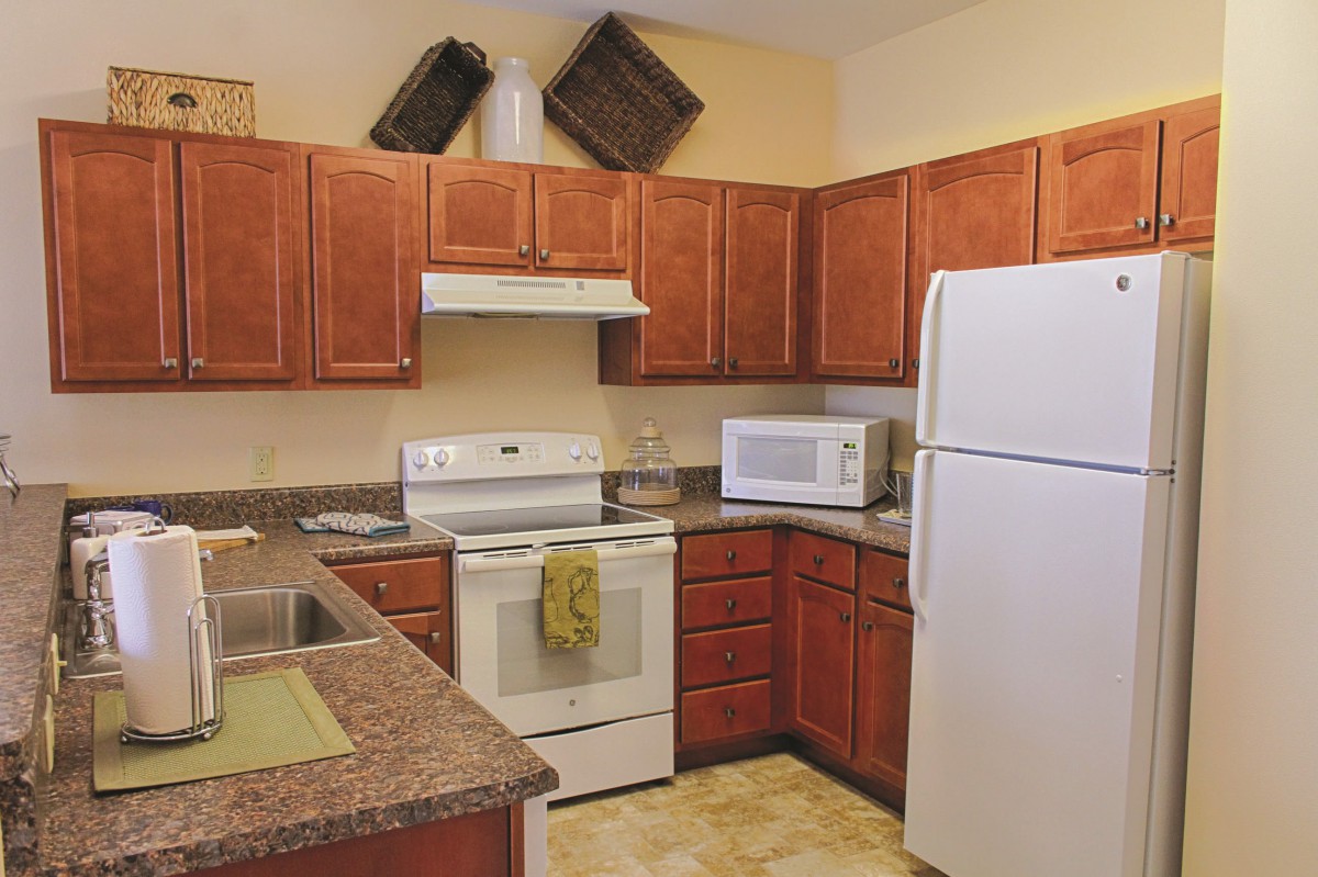 A cozy kitchen with wooden cabinets and modern appliances, including a refrigerator, oven, and microwave.