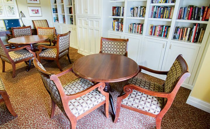 A cozy library space with a round wooden table surrounded by four patterned chairs, adjacent to bookshelves filled with books.