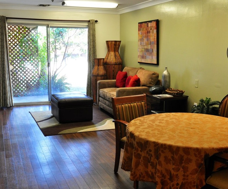 A cozy living room with a sofa, table, and wood flooring, featuring a sliding door leading outside.