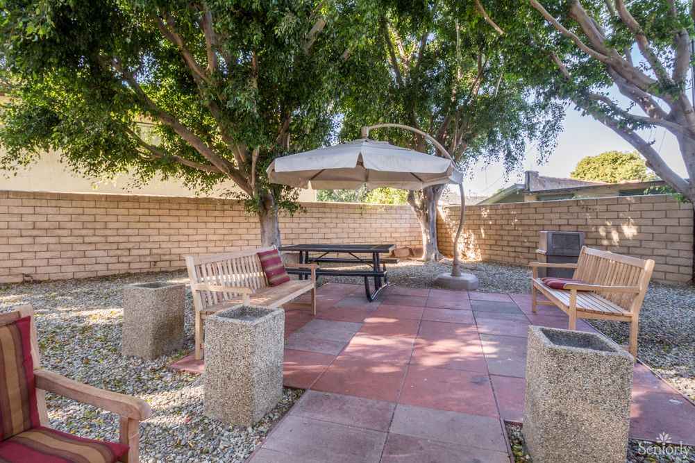 A cozy backyard patio with a picnic table and umbrella, surrounded by trees and a brick wall.