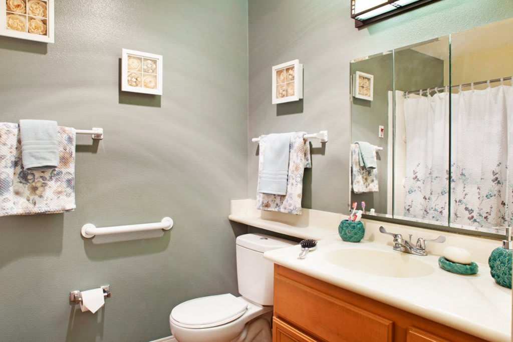 A neatly organized bathroom with a toilet, sink, and mirror, featuring decorative wall art and towels.