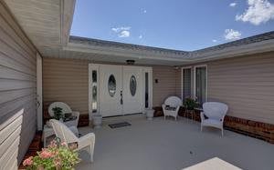 A cozy outdoor patio with white chairs and plants leading to a double door entrance.