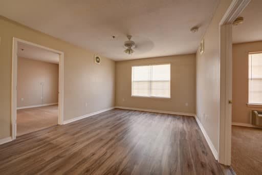 An empty room with hardwood flooring, a ceiling fan, and a window.