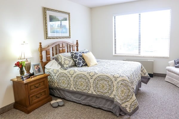 A cozy bedroom featuring a neatly made bed with patterned bedding, wooden headboard, and matching nightstand.