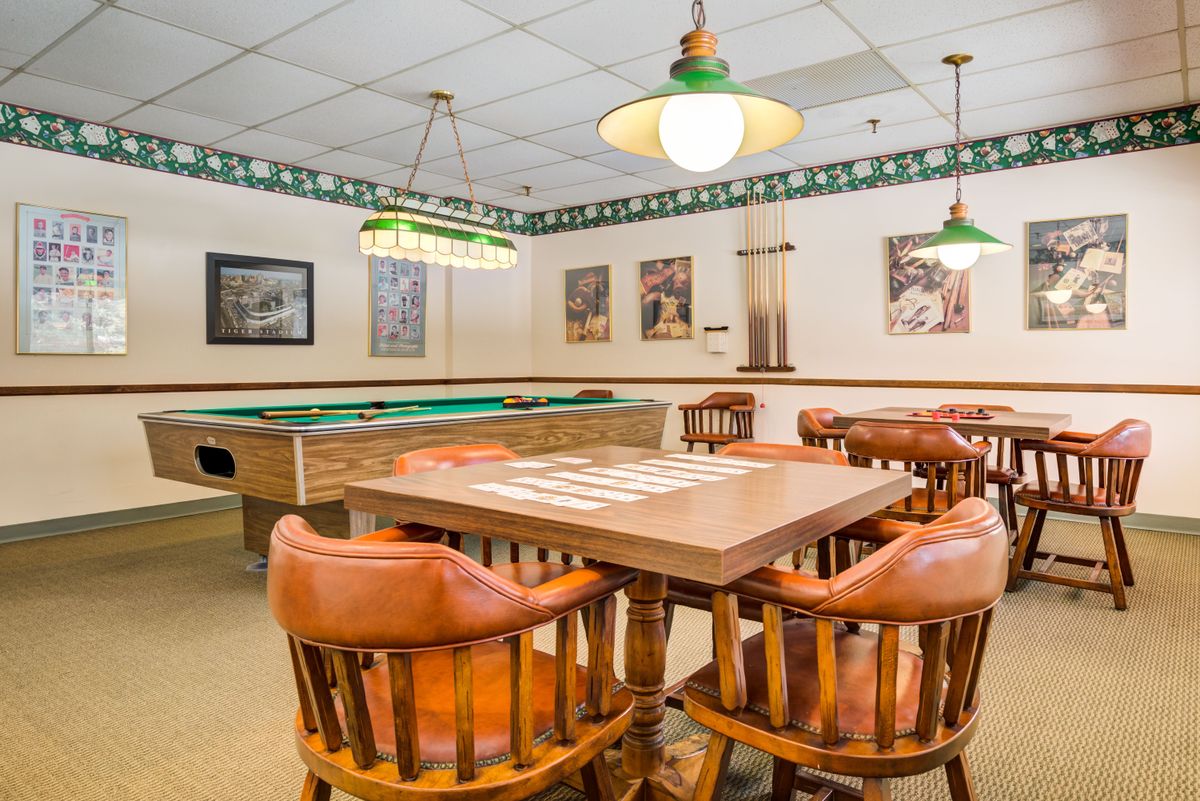 A cozy billiards room featuring a pool table and a wooden table with chairs, illuminated by hanging lights.