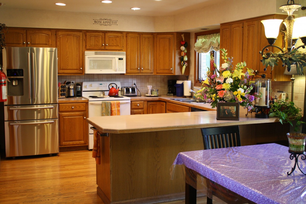 A modern kitchen featuring wooden cabinets, a central island with a countertop, and vibrant flower arrangements.