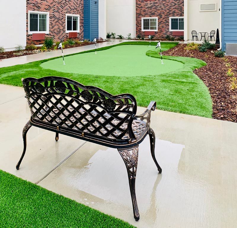 A neatly landscaped garden with a wrought iron bench and artificial grass.