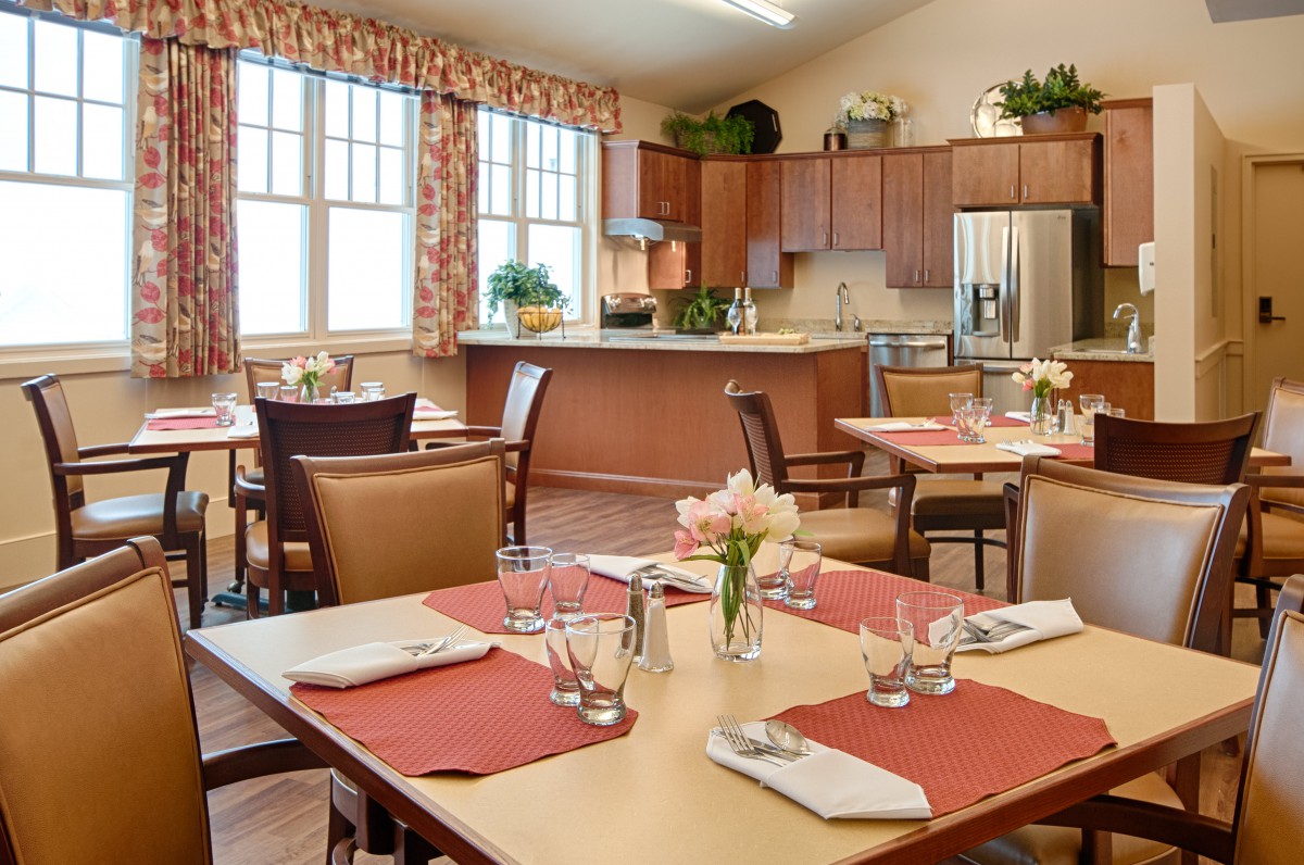 A well-set dining area with tables and chairs, adjacent to a kitchen space.