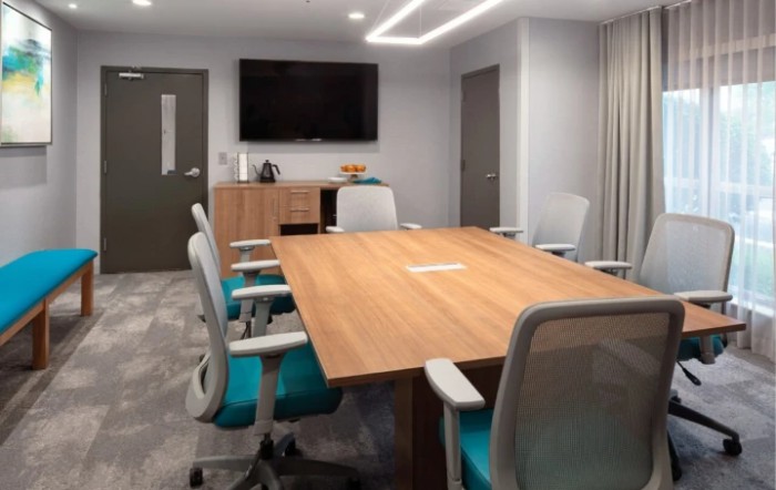 A modern conference room with a wooden table, ergonomic chairs, and a large TV screen.