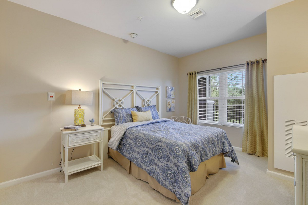 A cozy bedroom with a neatly made bed, nightstand, and a window with curtains.
