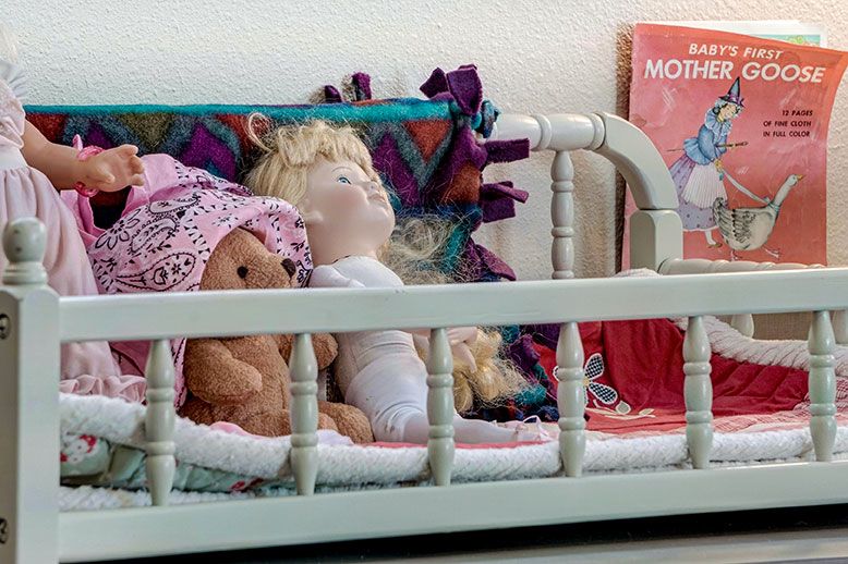 A doll and a teddy bear resting in a small toy bed with colorful blankets.