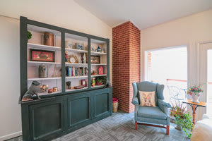 A cozy living room with a bookshelf and armchair by a brick chimney.