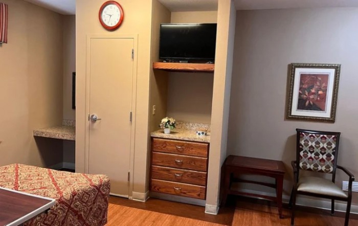 A cozy interior room with a wall-mounted TV, dresser, and analog clock.