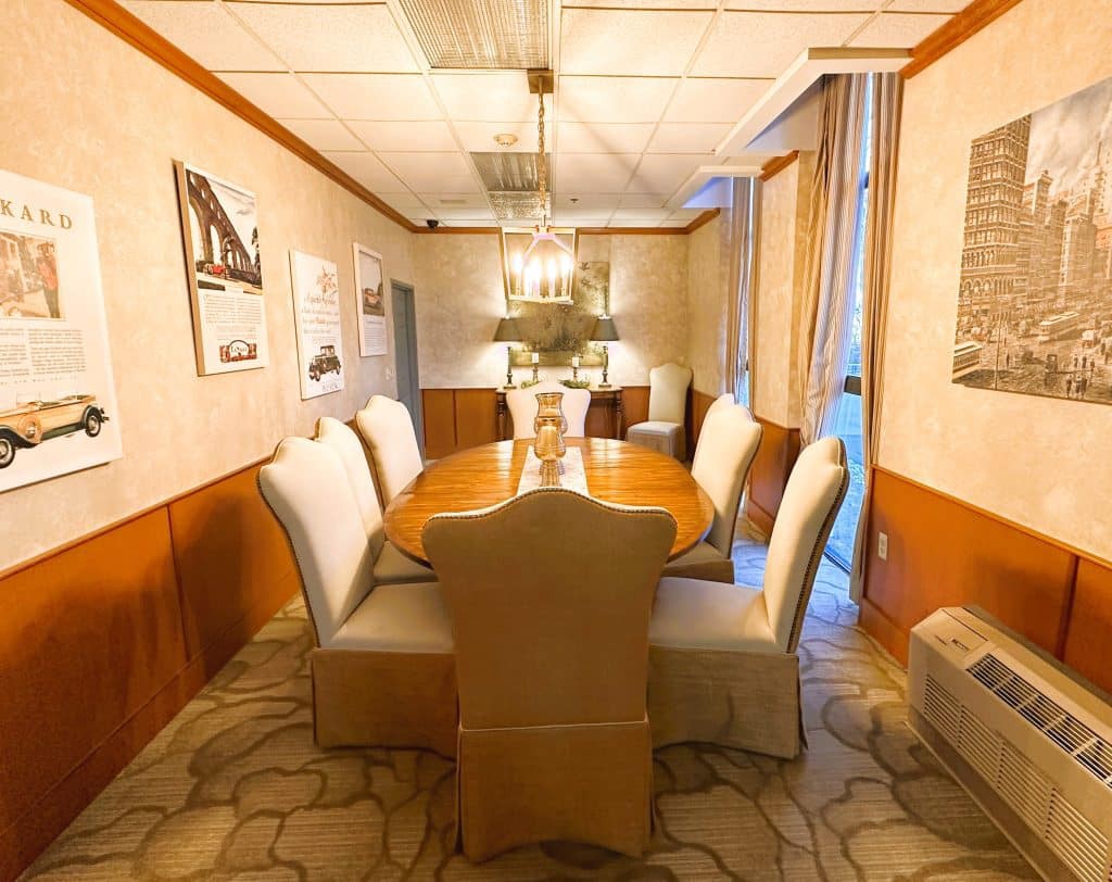 A well-lit dining room with a long table surrounded by upholstered chairs, adorned with artwork on the walls.