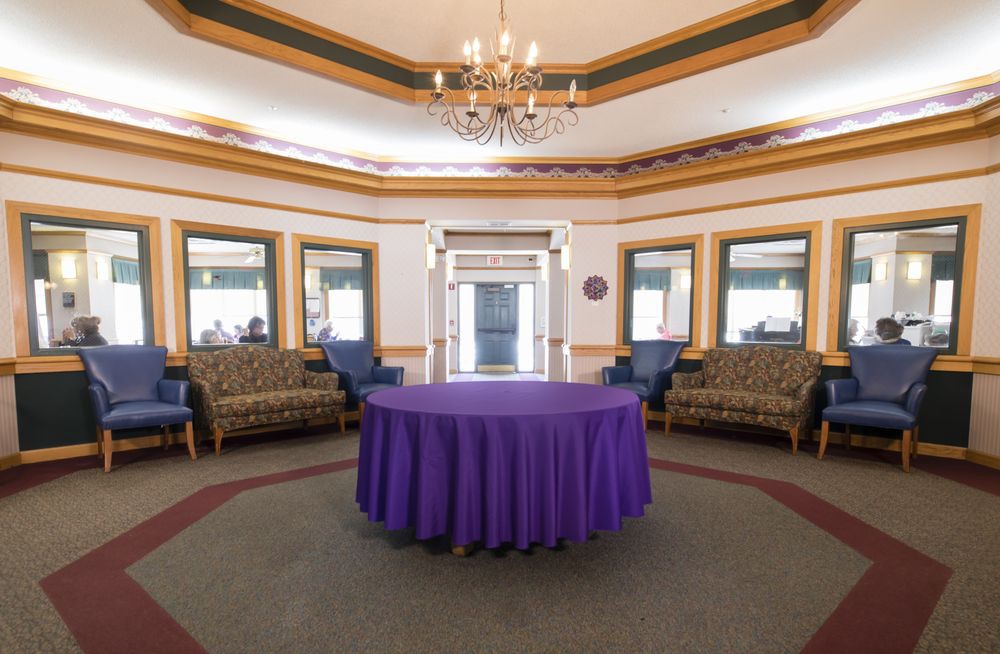 A well-decorated room featuring a round table with a purple tablecloth, surrounded by comfortable seating and illuminated by a chandelier.