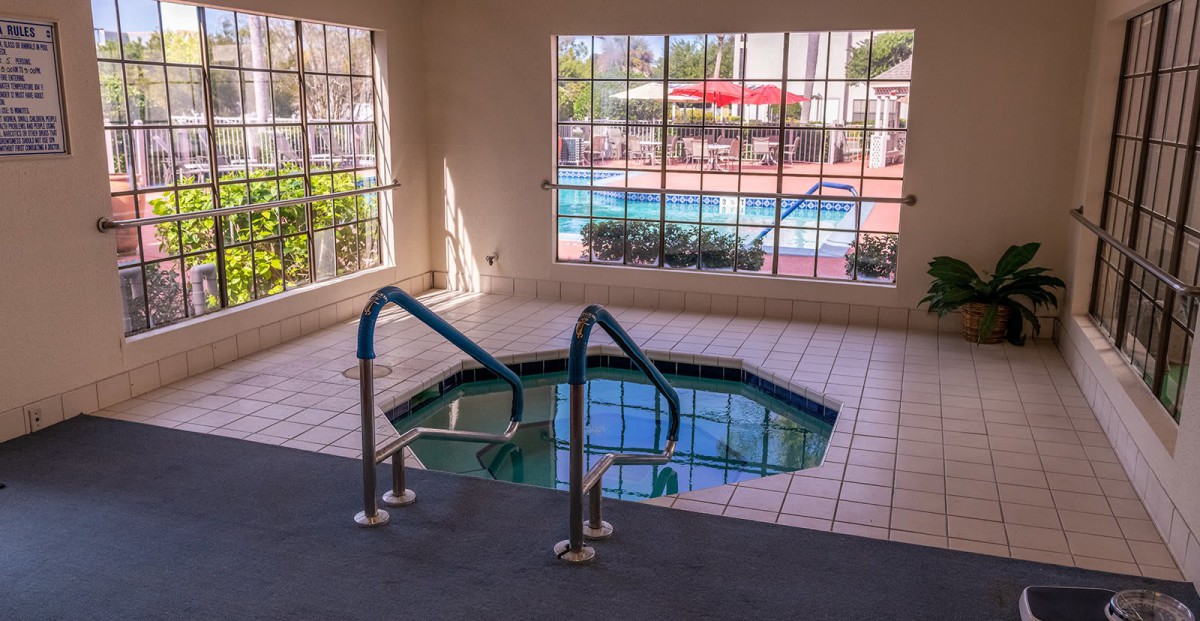 Indoor hot tub with a view of the outdoor swimming pool through large windows.