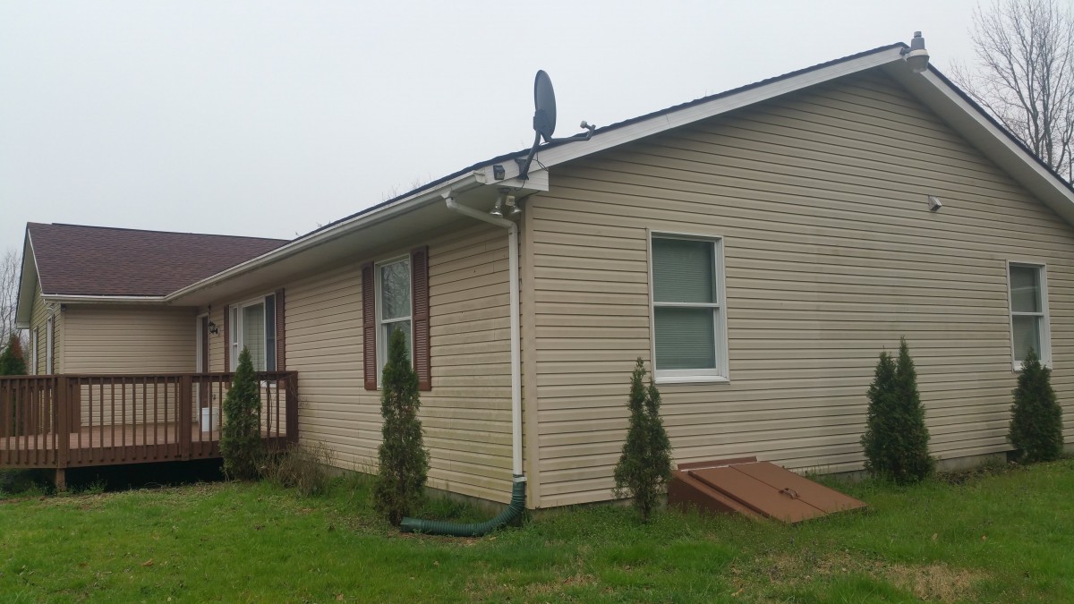 A single-story house with a satellite dish mounted on the roof and small bushes along the side.