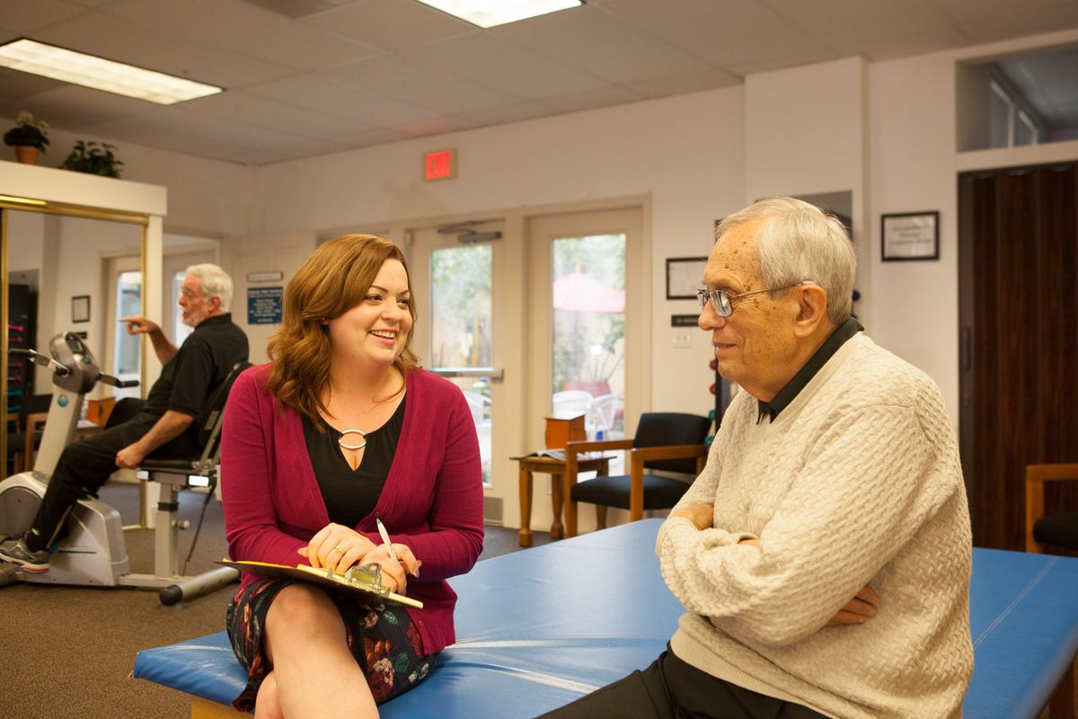 A woman and an elderly man are having a friendly conversation in an indoor setting.