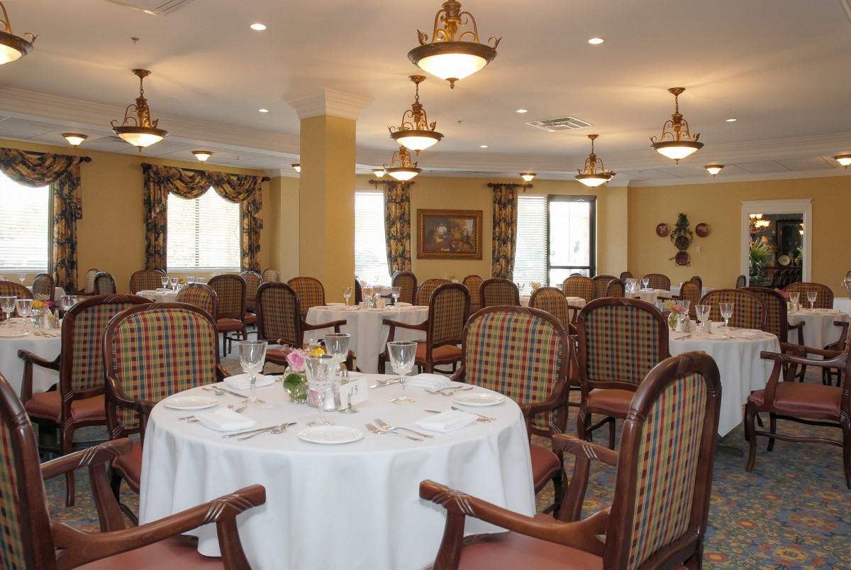 An elegant dining room with neatly arranged tables and chairs, illuminated by chandeliers.