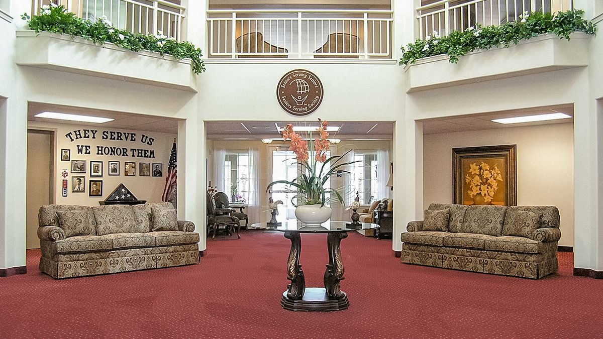 A spacious and elegantly decorated lobby with sofas, a central table holding a plant, red carpeting, and natural lighting.