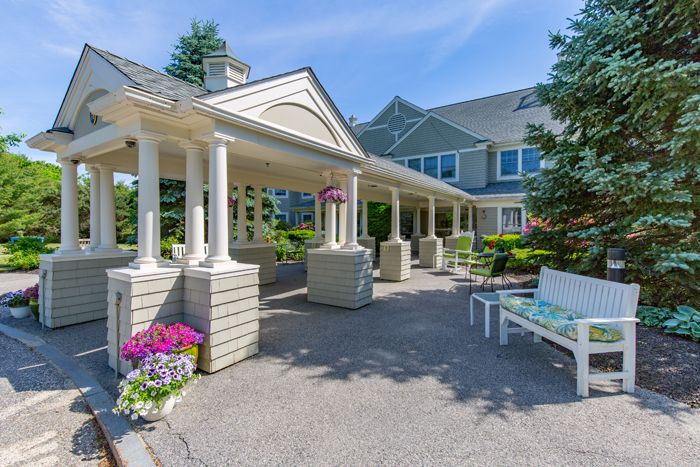 A well-maintained building entrance with columns, surrounded by flowers and a bench.