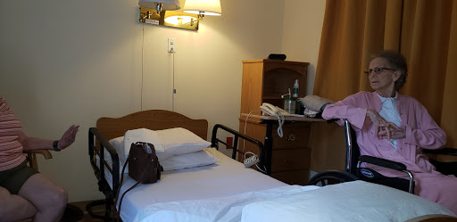 A simple hospital room with a bed, lamp, and a nightstand holding various personal items.