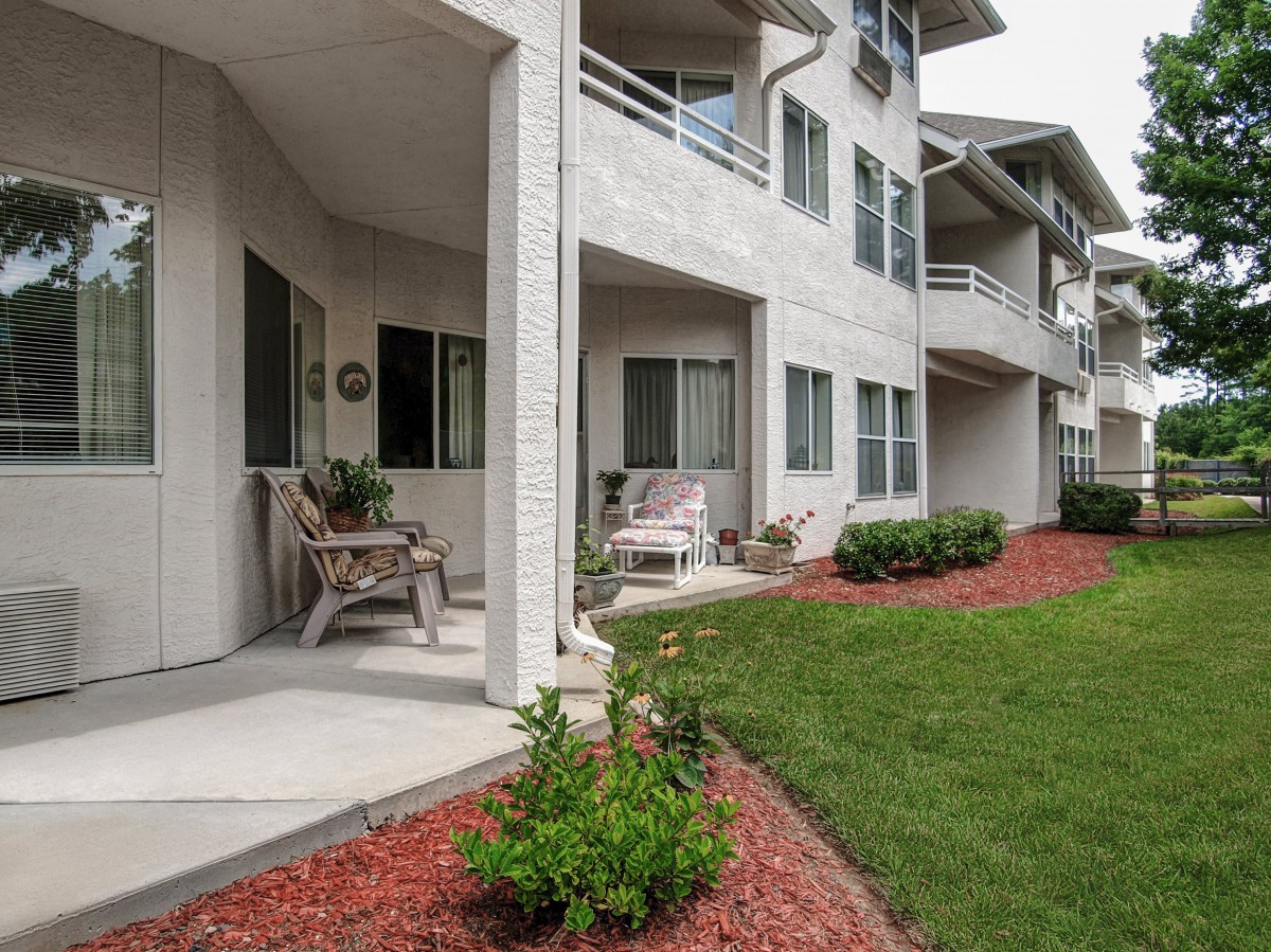 A view of an apartment building with patios and balconies overlooking a landscaped area with neatly trimmed grass.