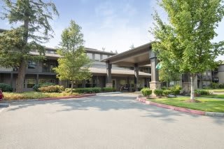 A spacious building entrance surrounded by trees and a curved driveway.