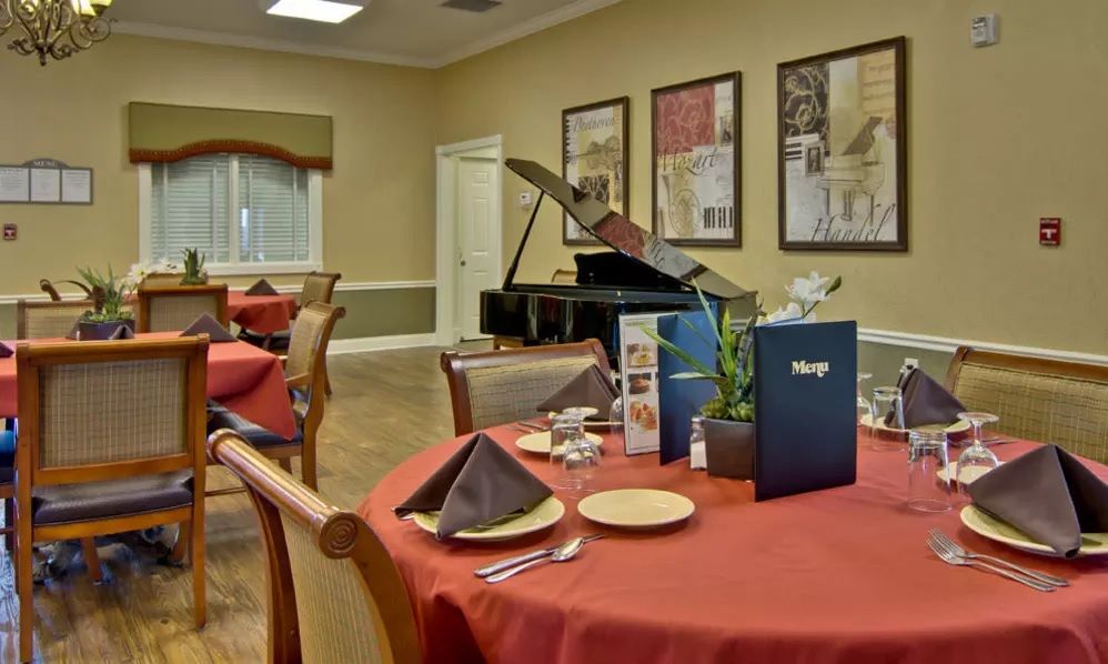 An elegant dining room featuring tables set with menus and a grand piano in the corner.