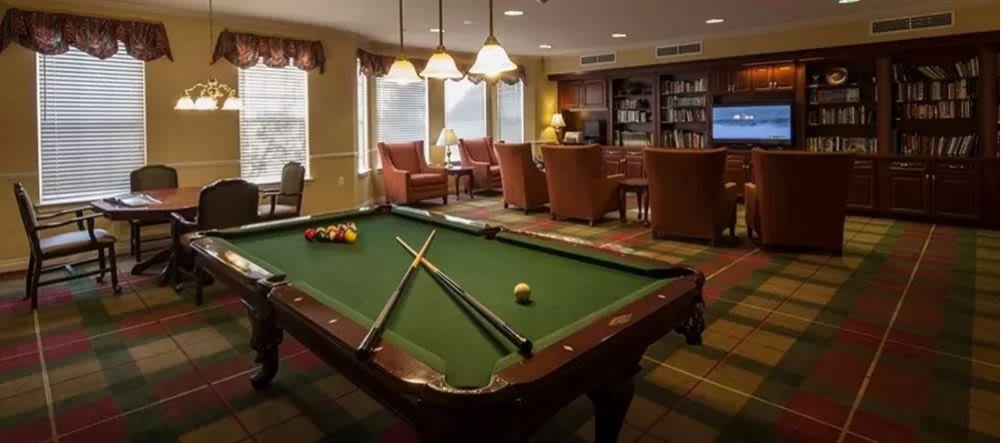 A cozy recreation room featuring a pool table, comfortable seating, and bookshelves.
