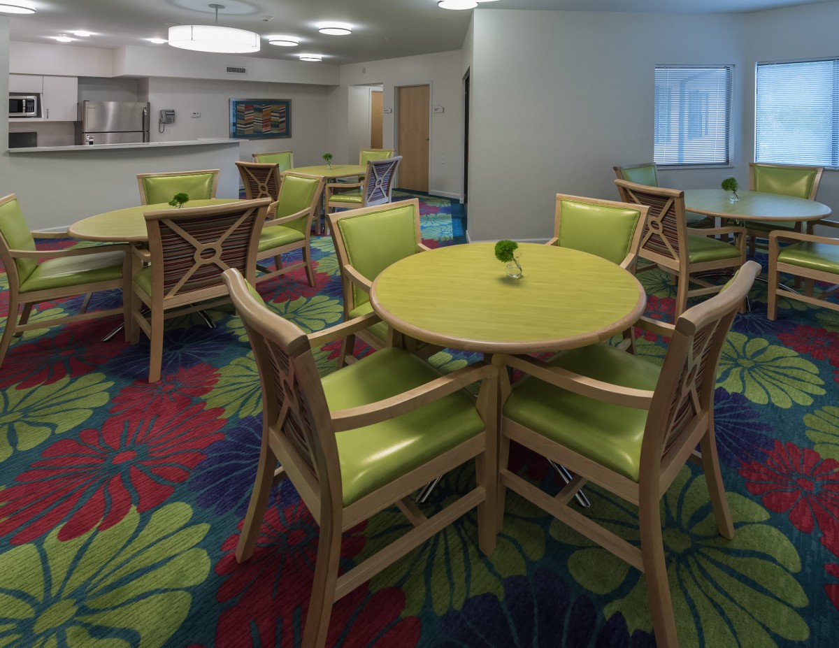 A modern dining area with green chairs and round tables set against a colorful carpet.