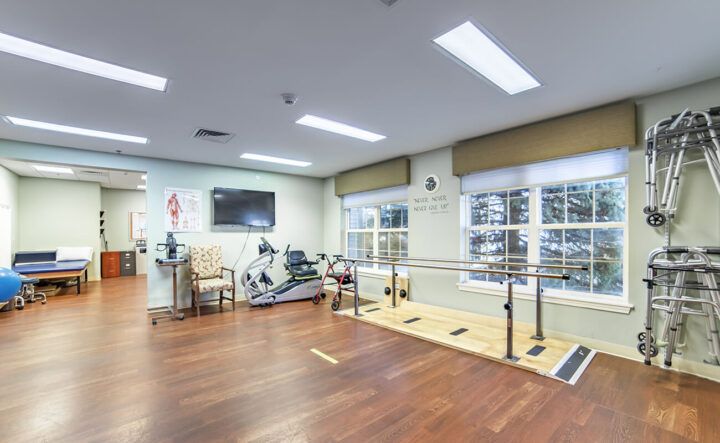 A spacious rehabilitation room with exercise equipment and parallel bars.