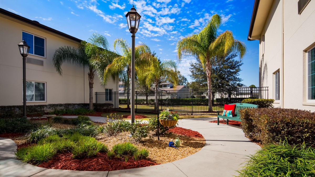 A scenic garden pathway lined with palm trees and outdoor seating under a bright blue sky.